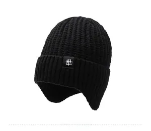Detail of black winter knit hat with earflaps and a white snowflake logo patch