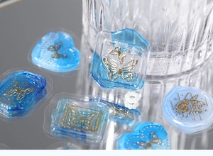 Close-up of clear blue wax seal stickers with gold butterfly relief on mirrored surface