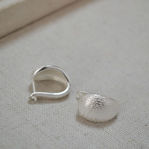 Macro detail of silver-finish earrings featuring a vintage hammered matte texture finish