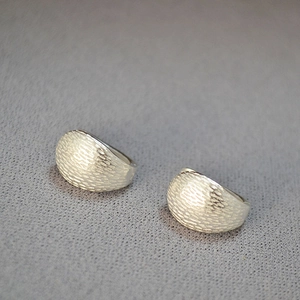 Macro detail of matte silver earrings featuring a brushed texture and minimalist oval shape