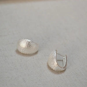 Close-up of matte silver U-shaped hoop earrings with brushed ripple texture on linen fabric