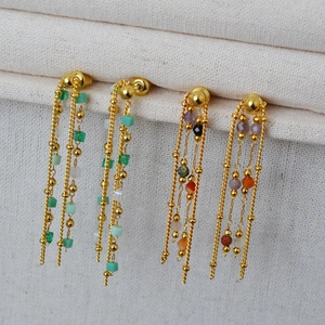 Close-up of gold beaded fringe earrings with colorful crystal accents on white fabric