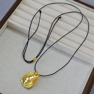 Détail du pendentif doré martelé avec cordon en cuir noir dans un écrin à bijoux