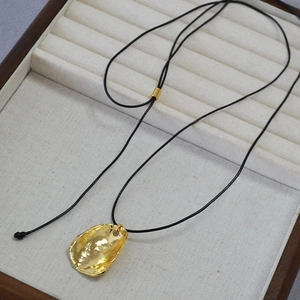 Détail du pendentif ondulé plaqué or avec cordon en cuir noir sur un coffret à bijoux chic