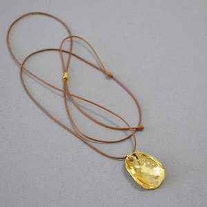 Gros plan du pendentif martelé doré sur un cordon marron réglable pour collier