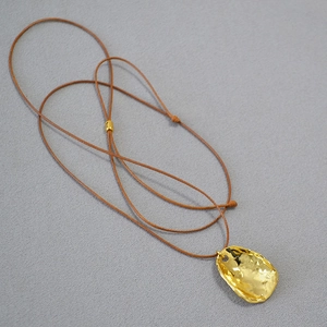 Détail d'un pendentif doré de forme organique avec texture martelée sur cordon brun