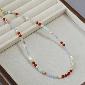 Detail of beaded necklace with red agate, blue stones, and white freshwater pearls