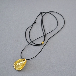Vue détaillée du pendentif doré martelé irrégulier sur un cordon noir minimaliste