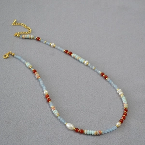 Detail of asymmetrical beaded necklace with blue stones, red beads and white pearls