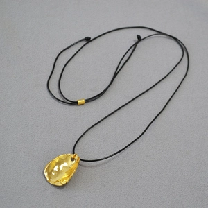 Détail du pendentif doré ondulé irrégulier avec cordon ciré noir sur une surface grise