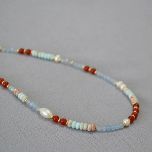Handmade necklace with red agate, pearls and blue stones on light gray fabric