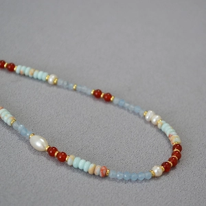 Macro detail of asymmetric necklace with blue stones, red agate, and white pearls
