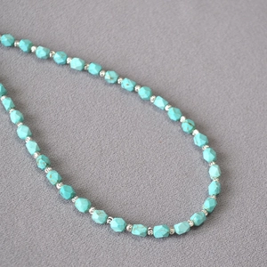 Macro shot of faceted turquoise beads with silver spacers on grey textured fabric