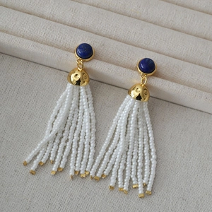 Detail view of long tassel earrings with blue lapis lazuli and white seed beads on a tray