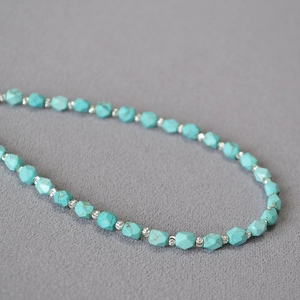 Faceted turquoise bead necklace with metallic spacers on dark grey textured background