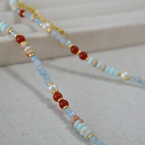 Macro shot of asymmetric necklace with blue stones, red agate, and white pearls