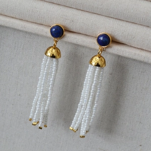 Close-up of lapis lazuli earrings with white beaded tassels and gold metal accents