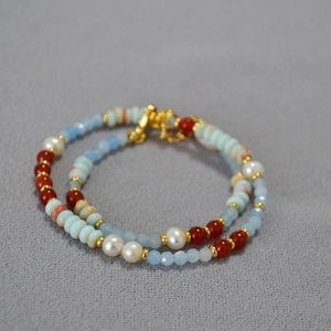 Detail of beaded necklace featuring blue stones, red agate, and white pearls on grey fabric