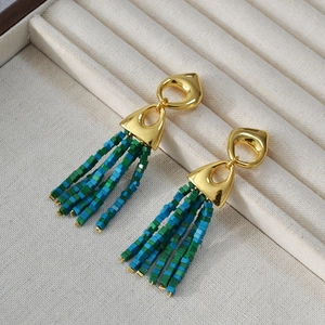 Detail of golden tassel earrings with green and blue square beads on beige tray