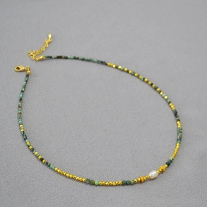 Detail of beaded necklace with faceted gold beads, turquoise stones, and a freshwater pearl