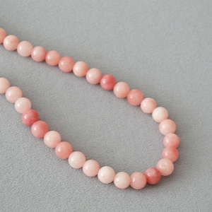 Detail of beaded necklace featuring smooth pink apatite round stones on textured cloth