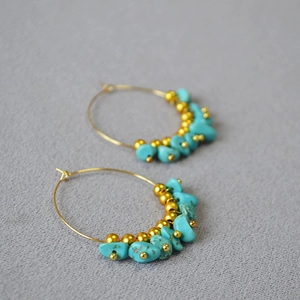 Detail of bohemian gold hoop earrings with turquoise chips and beads on grey fabric
