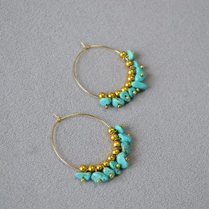 Detail of bohemian gold hoop earrings with turquoise stones and golden beads on grey fabric