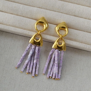 Detail of gold geometric stud earrings with purple square beaded tassels on a tray