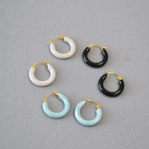 Close-up of three pairs of C-shaped enamel hoop earrings in white, blue and black with gold clips