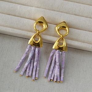 Detail view of retro gold earrings with lavender square bead tassels on a tray