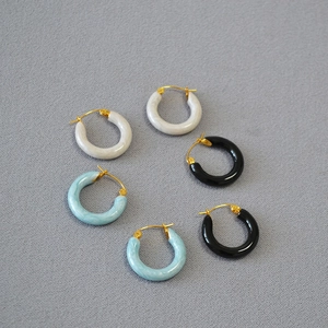 Detailed close-up of marble white, blue, and black hoop earrings on a gray fabric texture