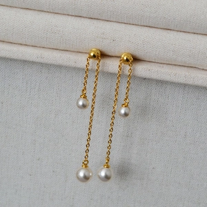 Macro shot of long gold tassel earrings with elegant white pearls on textured fabric