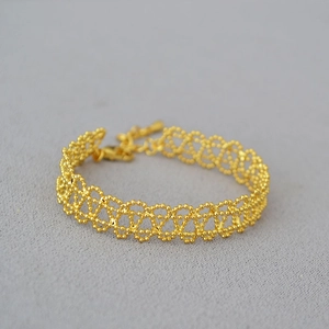Close-up of gold woven lace bracelet with intricate beadwork and lobster clasp detail