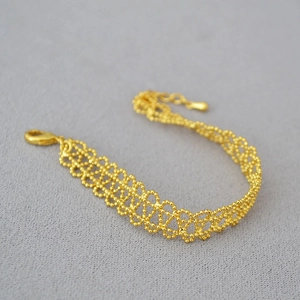 Close-up of gold beaded lace-style bracelet with intricate woven texture and lobster clasp