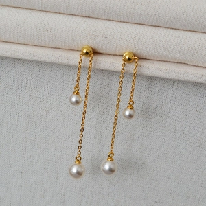 Detailed close-up of long gold pearl drop earrings on textured beige fabric