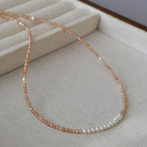 Detail of beaded necklace featuring orange natural stones and white freshwater pearls