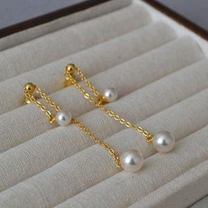 Detailed view of long gold chain earrings with layered white pearls in a jewelry box
