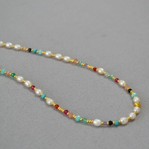 Gros plan de perles de pierres précieuses facettées et perles d'eau douce sur collier doré