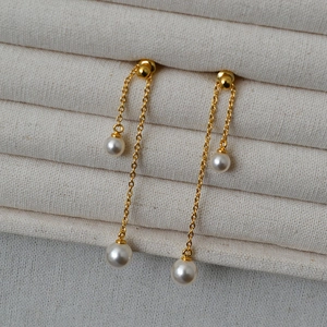 Macro shot of long golden tassel earrings with round pearls on a velvet display