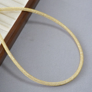 Macro detail of a shimmering gold mesh chain necklace with a frosted glitter texture finish