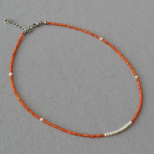 Close-up of beaded necklace with orange faceted beads and natural freshwater pearls