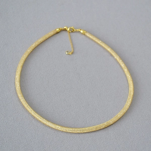 Macro detail of gold plated mesh necklace with fine texture and lobster clasp closure