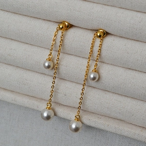 Detail of long gold chain tassel earrings with glossy white pearls on a display stand