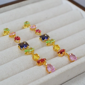 Macro detail of gold-plated drop earrings featuring multi-color faceted gemstones