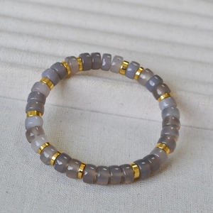 Macro detail of gray agate beads with golden spacers on a textured jewelry display