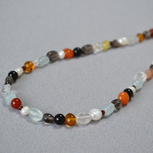 Detail of irregular natural gemstones and pearls necklace on grey textured fabric