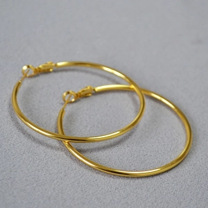 Detailed close-up of golden oversized C-shaped hoop earrings on a grey fabric