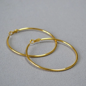 Close-up of oversized minimalist golden C-shaped hoop earrings on textured grey fabric