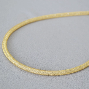 Macro shot of gold mesh-woven tube necklace showing intricate metallic wire texture
