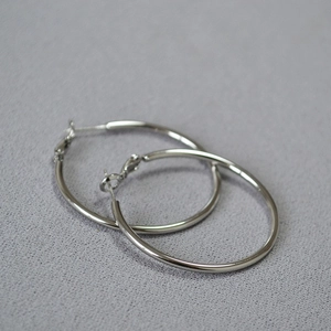 Detailed view of large polished silver C-shaped hoop earrings on gray fabric